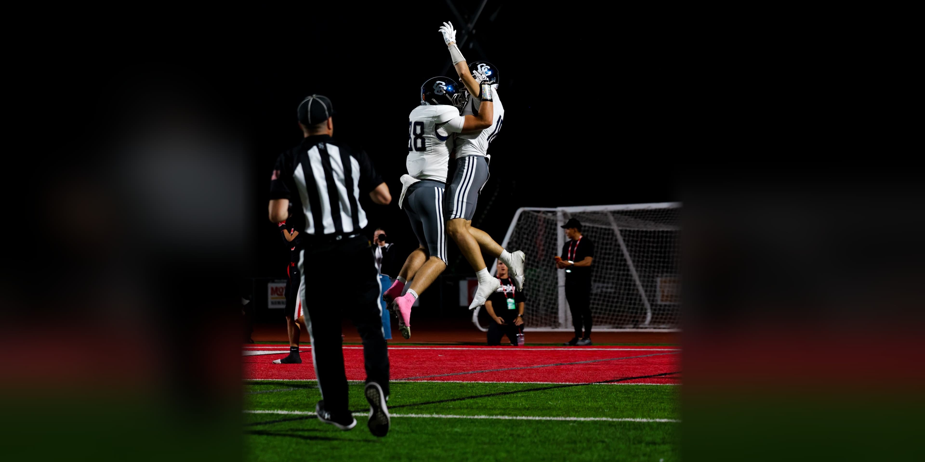 Two Corner Canyon players leap to celebrate a touchdown in the end zone at American Fork High School on October 8, 2026, as an official runs in.